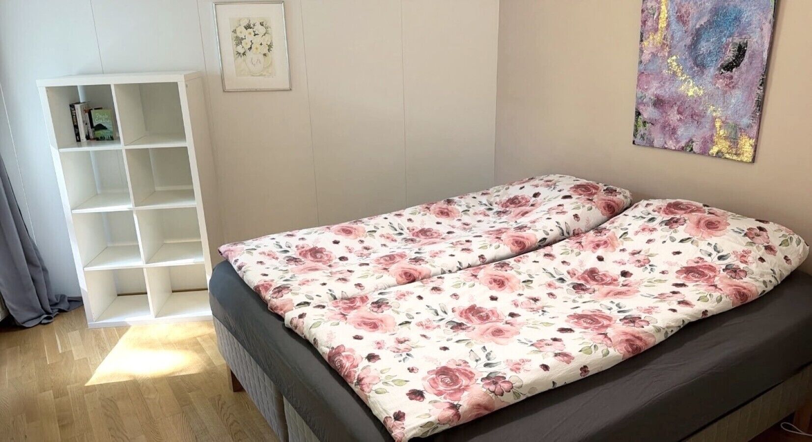 Une chambre à coucher avec un lit, une étagère blanche et un tableau floral accroché au mur.