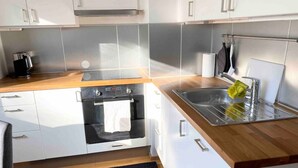 Une cuisine moderne avec des meubles blancs, un four en acier inoxydable, un évier et un plan de travail en bois.
