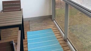 Un balcon avec une table et des chaises en bois, un tapis bleu et une vue sur un lac et des arbres.