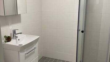 A bathroom with a white sink, mirror, and toilet. It has a glass shower enclosure and a beige rug on the floor.