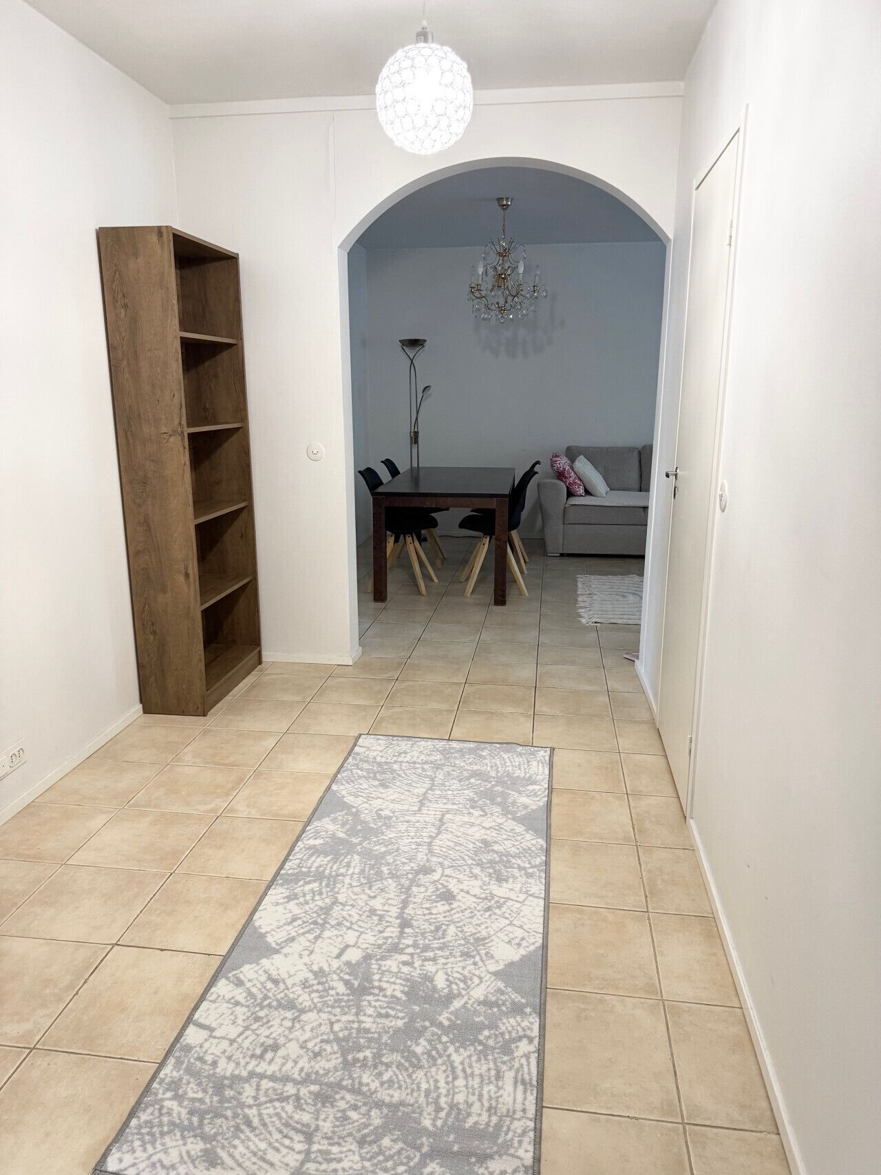 A spacious room with a dining table, chairs, a sofa, and a large wooden bookshelf.