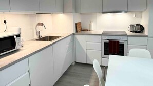 Une cuisine moderne avec des meubles blancs, un four à micro-ondes, un évier, une cuisinière et un coin repas comprenant une table et des chaises blanches.