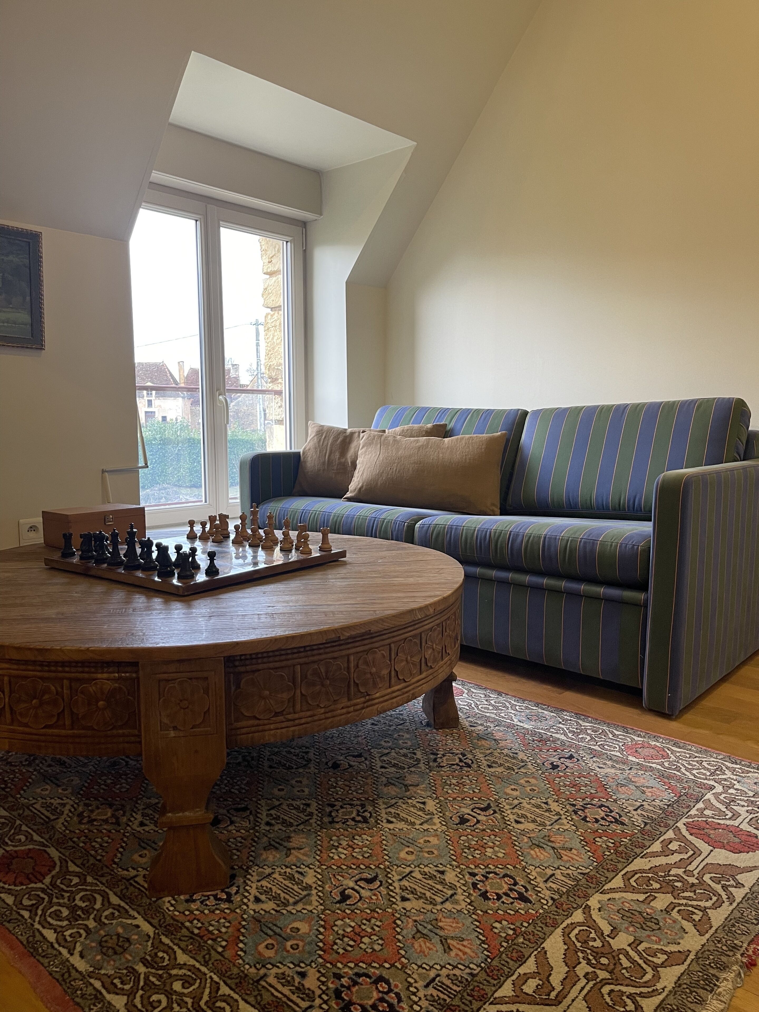 Una sala de estar acogedora con una mesa redonda de madera, un sofá a rayas y un tablero de ajedrez.