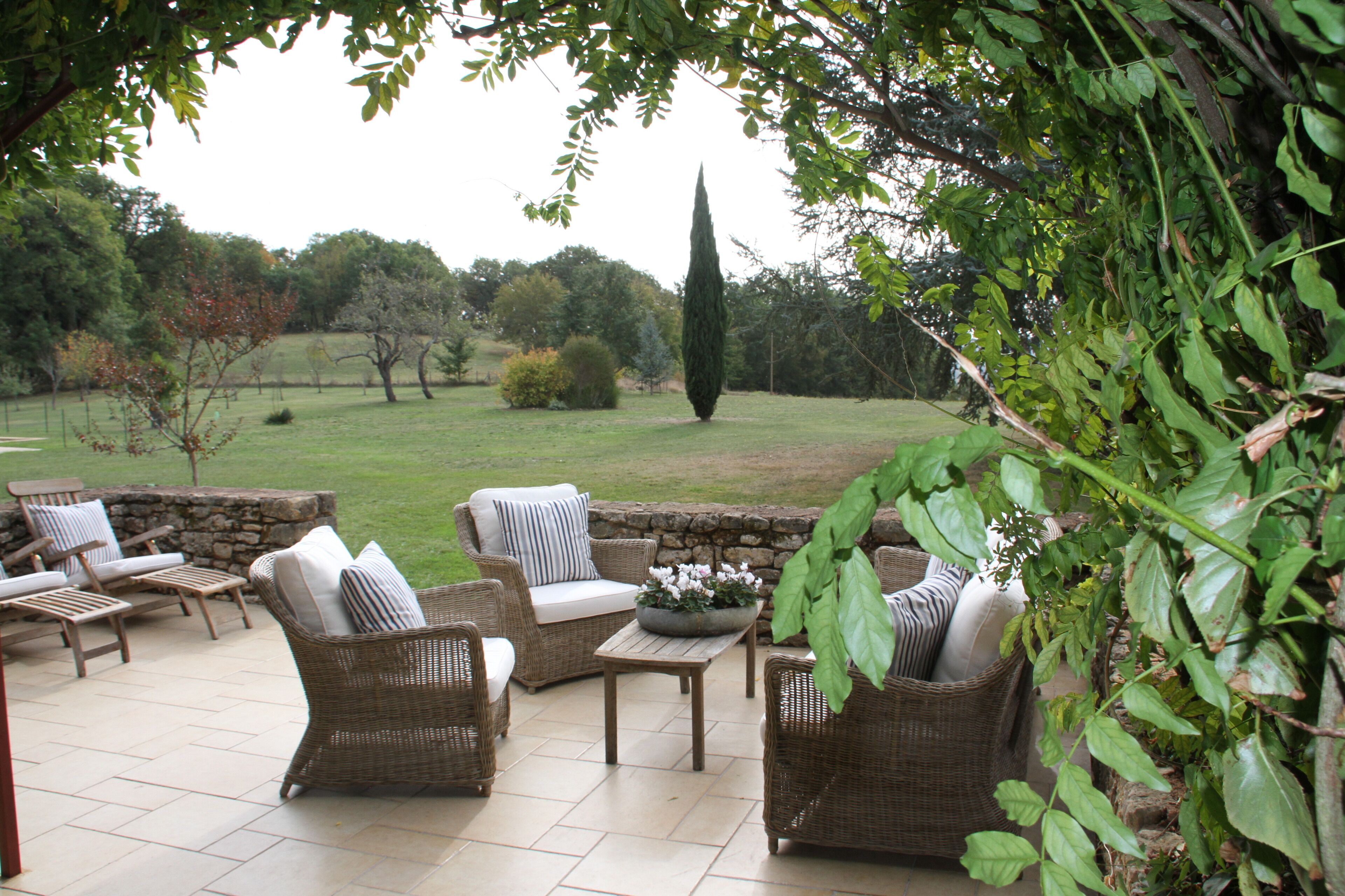 An outdoor patio area with wicker furniture, a stone wall, and a view of the surrounding landscape.
