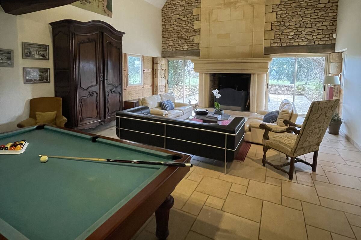 A cozy living room with a pool table, comfortable seating, a stone fireplace, and a large window.