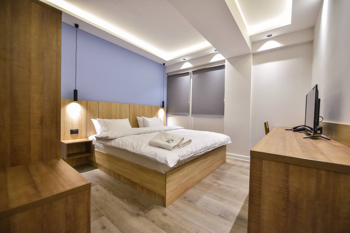 A modern bedroom with a wooden bed, bedside tables, and a desk with a computer.