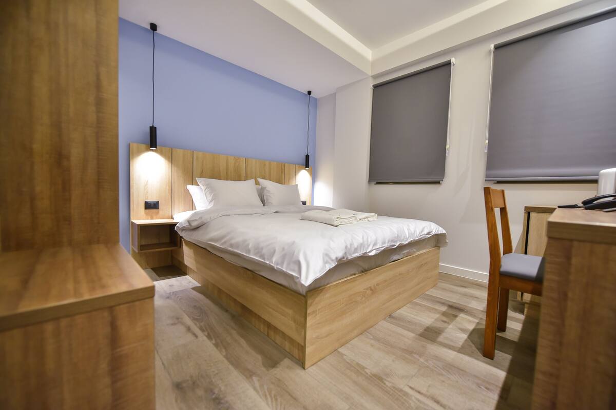 A modern bedroom with a wooden bed, bedside tables, a desk, and a chair.