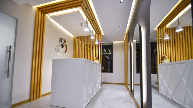 Una recepción moderna con un mostrador blanco, detalles de madera y un espejo grande.