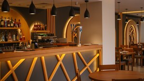 Una zona de bar con mostrador de madera, estantes con botellas, una máquina de café y lámparas colgantes.