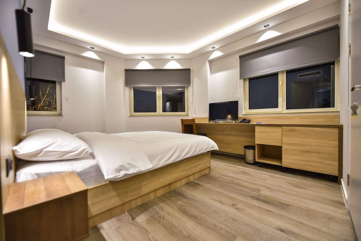 A modern bedroom with a wooden bed, built-in desk, and large windows.