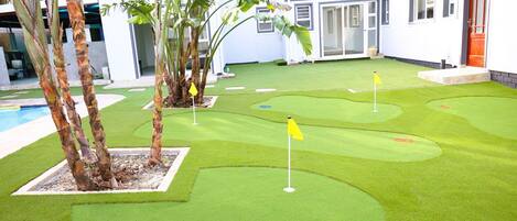 A miniature golf course with artificial grass, a pool, and a white building with a red door.