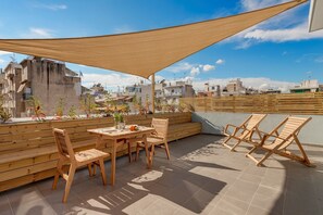 A rooftop terrace with wooden furniture, a table with a vase and fruit, and a view of the cityscape. - Executive Apartment With Private Terrace-d (Piraeus)