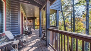 A wooden deck with Adirondack chairs and picnic tables, overlooking a forested area.