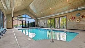 An indoor swimming pool with wooden ceiling and walls, clear windows, and lifebuoys on the wall.