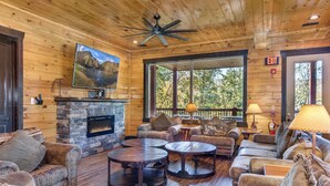 L’intérieur chaleureux d’un chalet en bois, avec une cheminée en pierre, des canapés en cuir et une grande fenêtre donnant sur le paysage extérieur.
