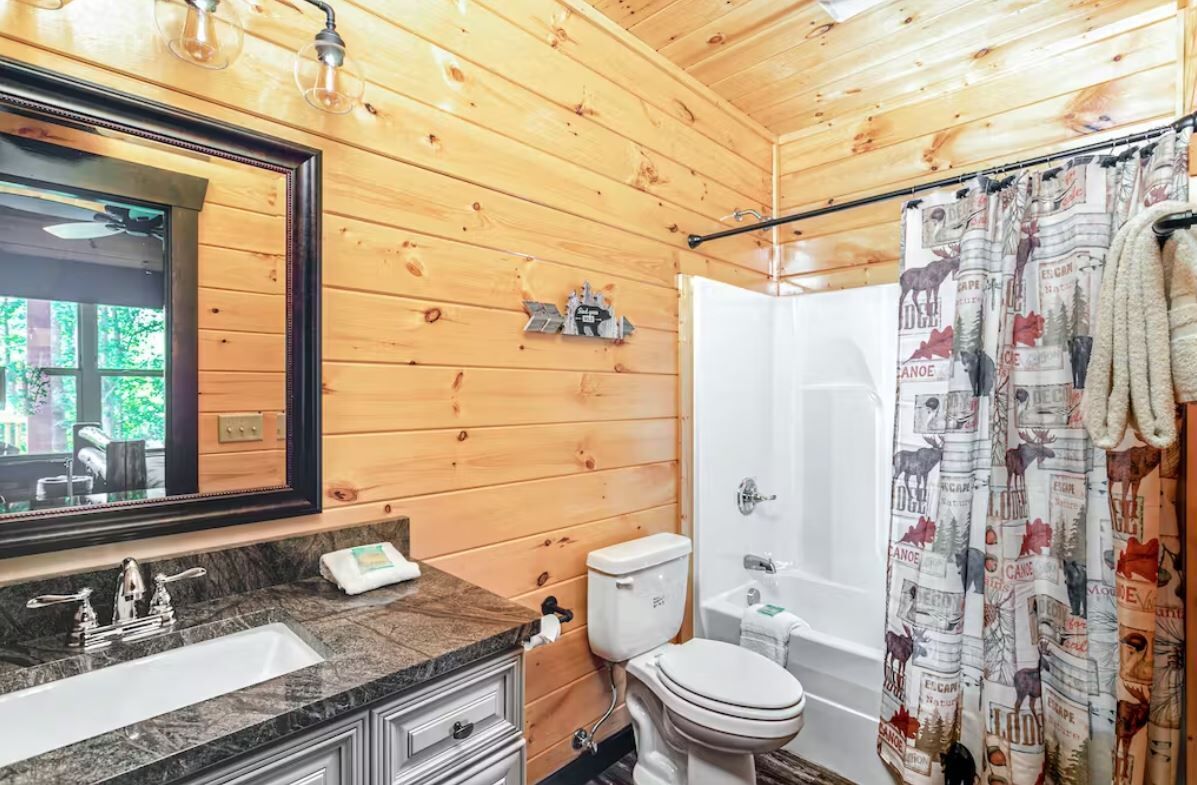 A wooden cabin bathroom with a large mirror, a sink, toilet, and a shower.