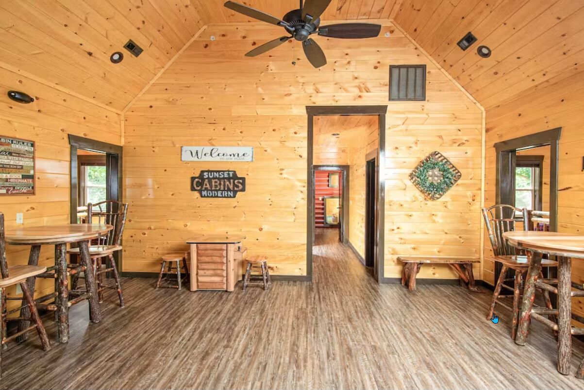 L’intérieur d’un chalet en bois, avec des meubles rustiques, un ventilateur de plafond et une pancarte « Bienvenue ».