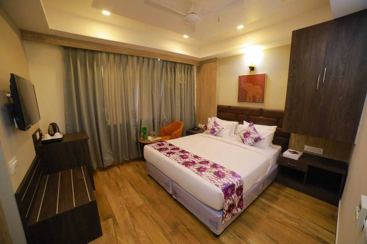 A hotel room with a large bed, a desk, a chair, a TV, and a wardrobe.