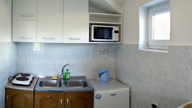 Una cocina compacta con armarios blancos, un microondas, un hervidor y un refrigerador pequeño.