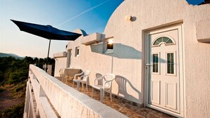 Un edificio con fachada blanca, una puerta con ventanal semicircular y un balcón con sillas y un paraguas azul.