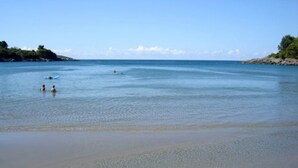 Una playa con agua tranquila, algunas personas a lo lejos y una costa rocosa con árboles.