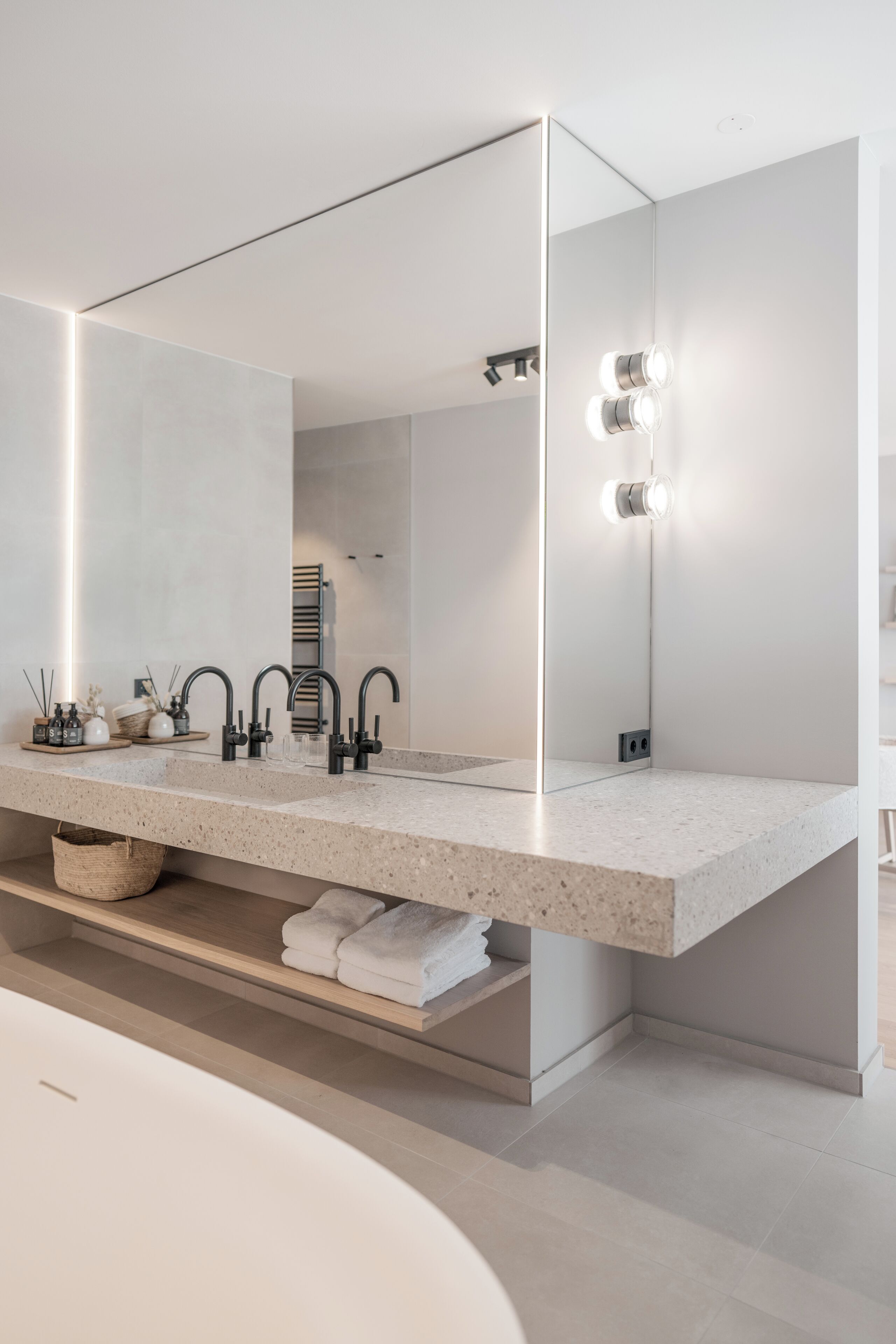A modern bathroom with a large mirror, two sinks, and a built-in shelf with towels.