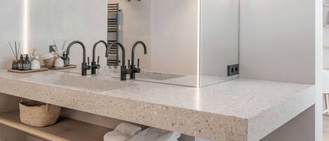 A modern bathroom with a large mirror, two sinks, and a built-in shelf with towels.