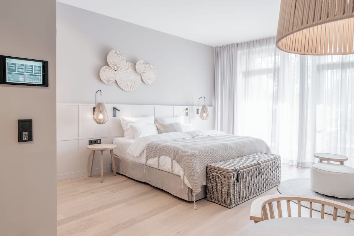 Un dormitorio moderno con cama, mesitas de noche, una cesta de mimbre y un pequeño rincón de descanso.