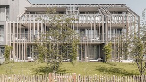 A modern multi-story building with balconies, a wooden fence, and a grassy lawn.