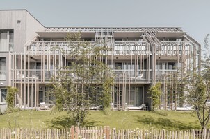 Un edificio moderno de varios pisos con balcones, cerca de madera y un jardín césped.