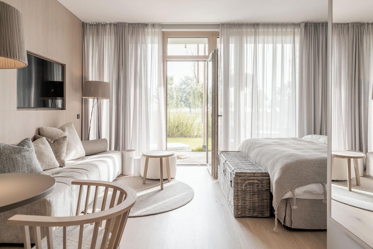 Un dormitorio moderno con sofá, cama, mesa de comedor y un amplio ventanal con cortinas.