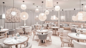 A modern dining area with round tables and chairs, featuring woven pendant lights and a neutral color palette.