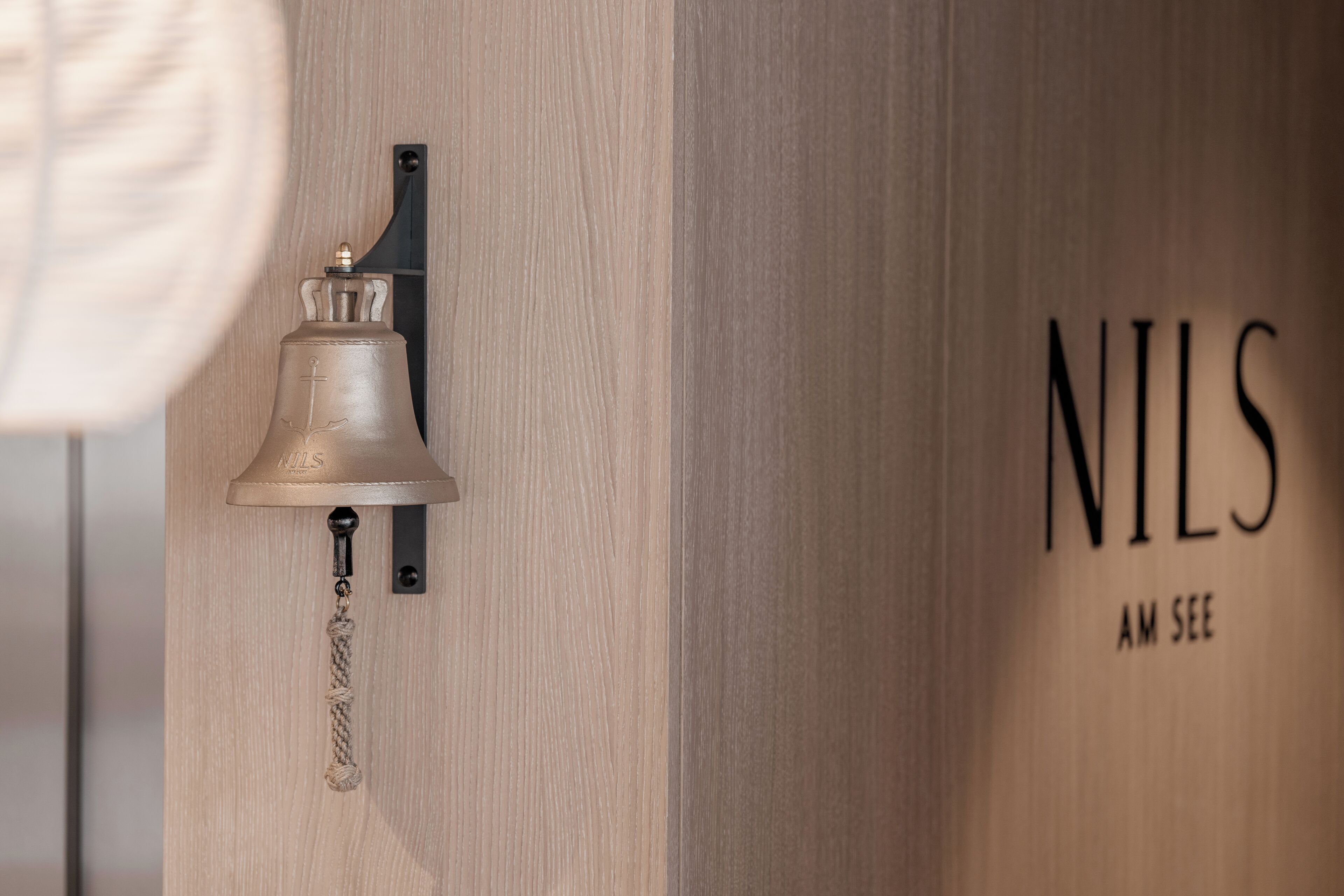 Pared de madera con una campana y el texto "NILS AM SEE".