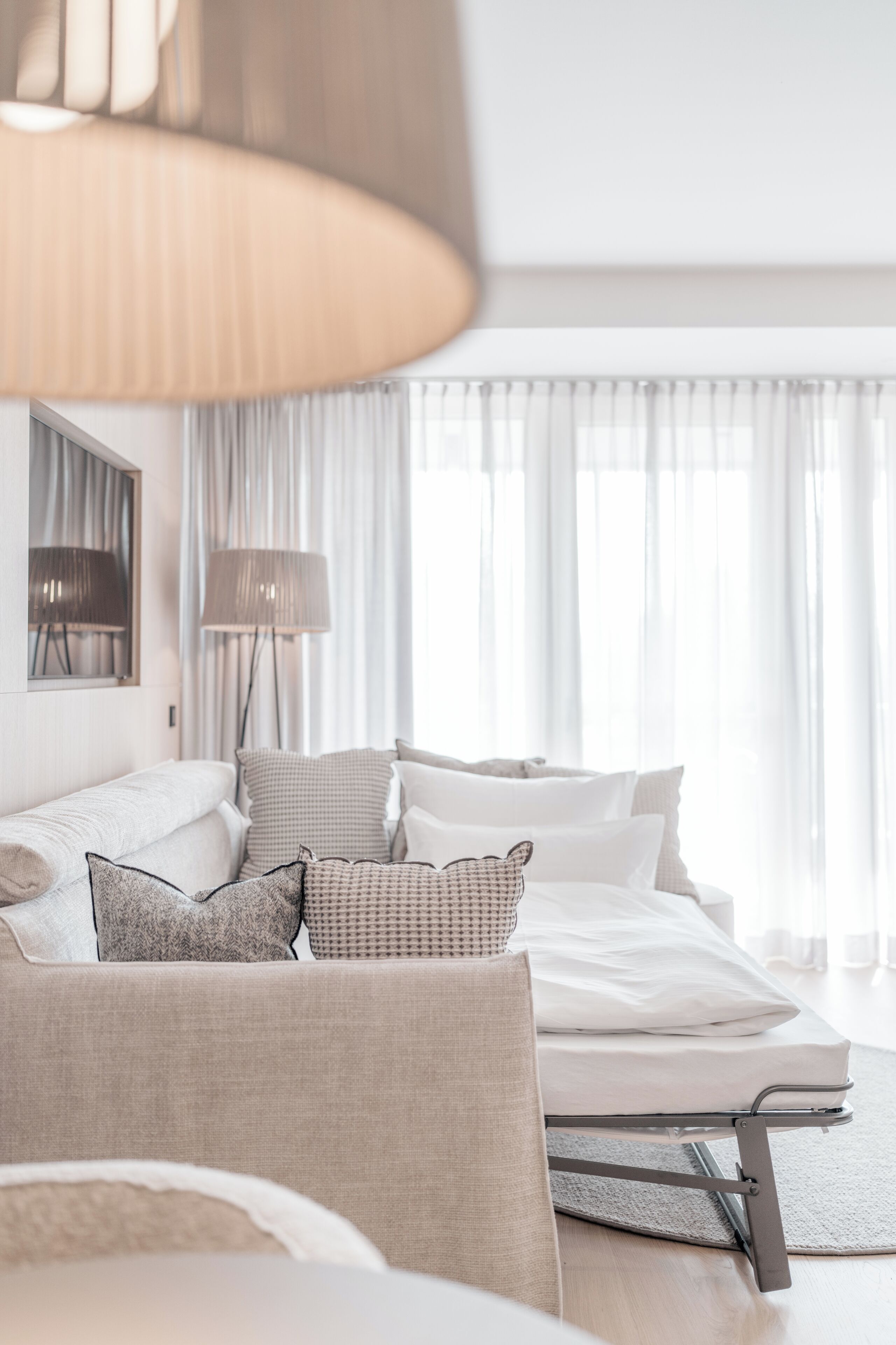 Une chambre d’hôtel moderne, équipée d’un lit, d’un canapé, d’une lampe et offrant une vue sur l’extérieur à travers de fines rideaux.