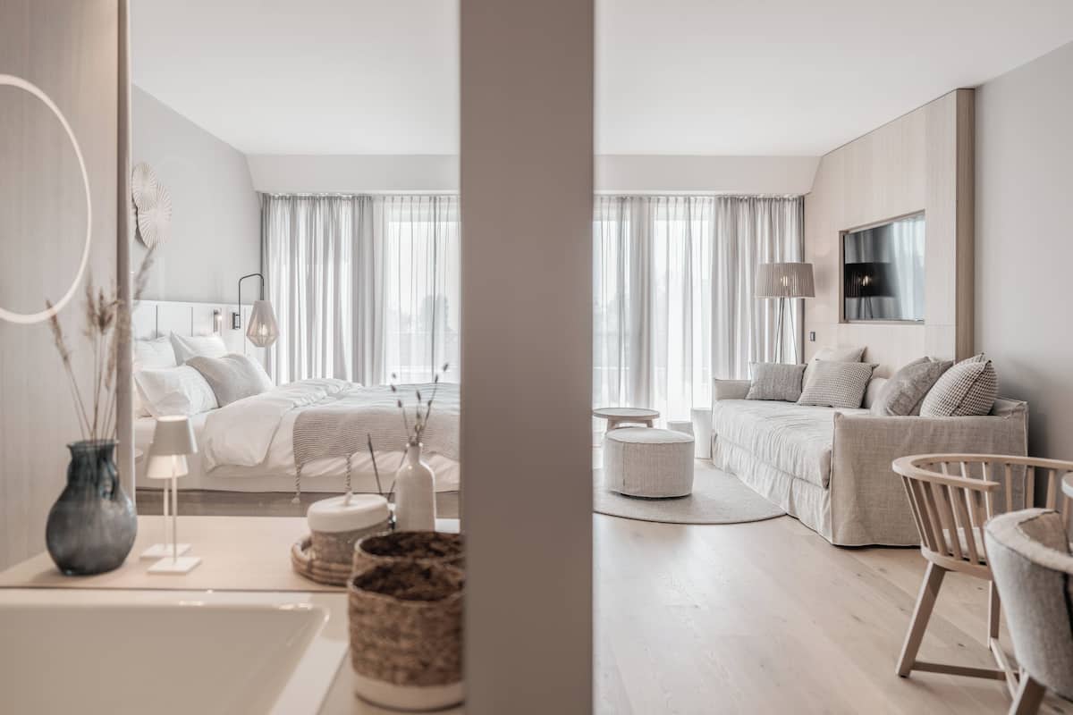 Una habitación de hotel moderna con una cama, un sofá, una silla, una lámpara y un televisor.