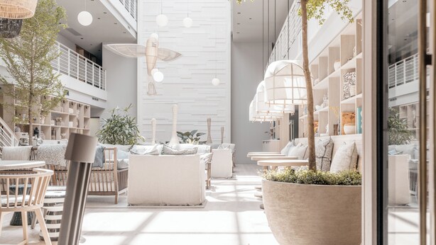 A spacious, modern interior with high ceilings, a central seating area with sofas and chairs, and a large planter with greenery.