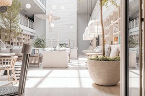 Un interior espacioso y moderno, con techos altos, una zona de estar central con sofás y sillones, y una maceta grande con plantas.