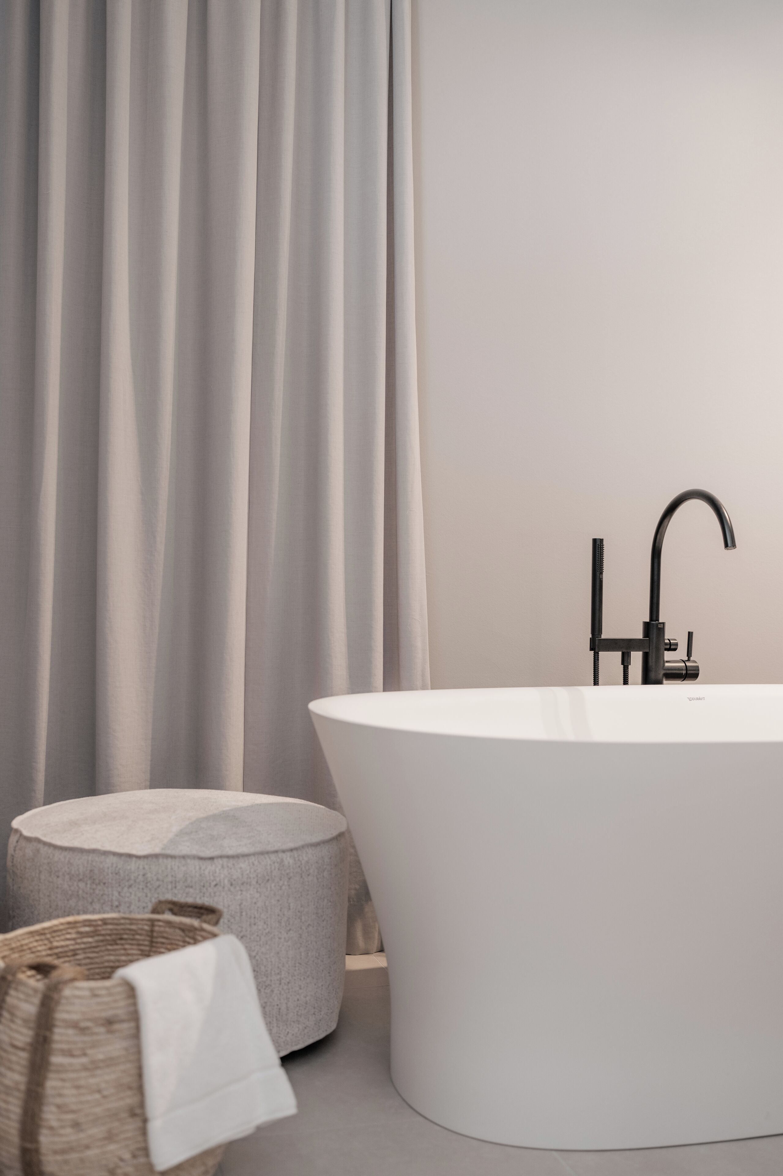 A modern bathroom with a freestanding bathtub, a round stone bench, and a woven basket.