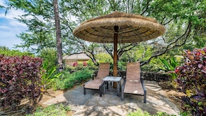An outdoor seating area with a thatched umbrella, surrounded by lush greenery and a stone pathway. - 🏖️Kulalani Townhome w/ Mountain Views + Beach Club Access (Kamuela)