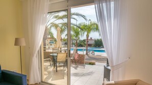 A room with a sliding glass door leading to a pool area, a sofa, and a lamp. - Narcissos Nissi Beach Apartment C3 (Ayia Napa)