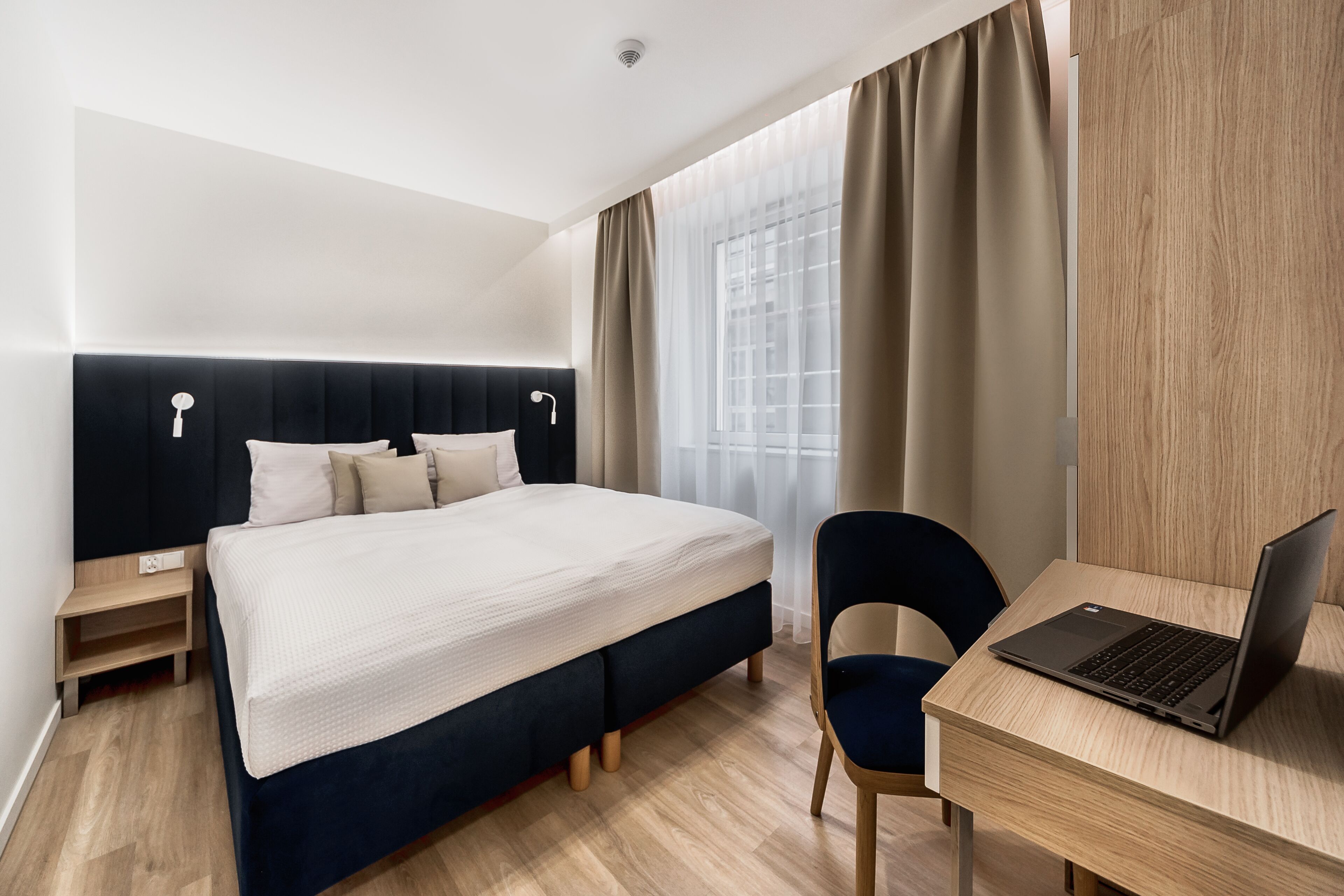 Een moderne hotelkamer met een bed, een bureau met een laptop en een stoel.