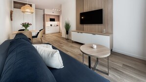 Un soggiorno moderno con un divano, un tavolino rotondo, una TV montata su una parete in legno e una cucina sullo sfondo.