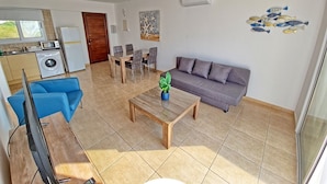Una sala de estar con sofá, mesa de centro, televisor y un comedor con sillas y mesa.