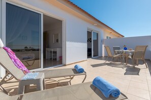 A sunlit outdoor patio with lounge chairs, a table, and a sliding glass door leading to an interior space. - Narcissos Nissi Beach Apartment C16 (Ayia Napa)