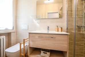 Ein modernes Badezimmer mit Toilette, einem Holzstuhl, einem großen Spiegel und einer Duschkabine aus Glas.