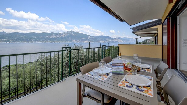 Ein Balkon mit Tisch für zwei Personen, mit Blick auf einen See und Berge.