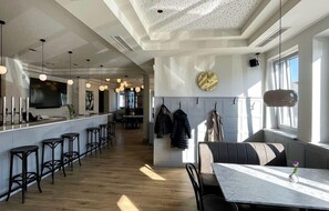 A modern restaurant interior with a long bar, multiple seating areas, and a large mirror on the wall. - Luis von Weyden (Weiden am See)