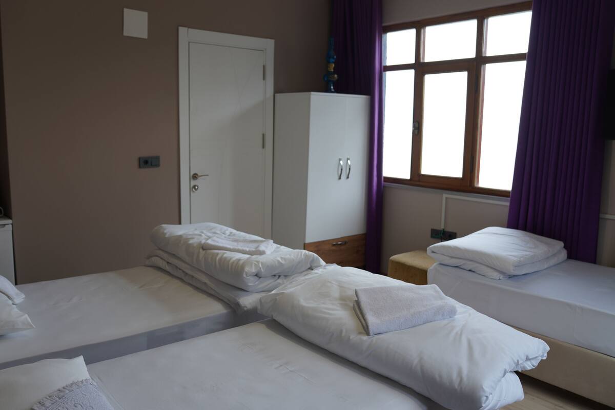 A hotel room with two beds, a wardrobe, a small table, and a window with curtains.