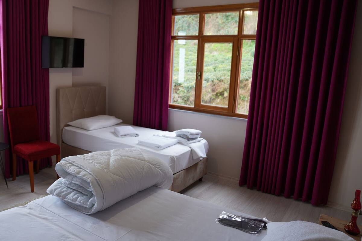A hotel room with a bed, a chair, a desk, a TV, and large windows with curtains.