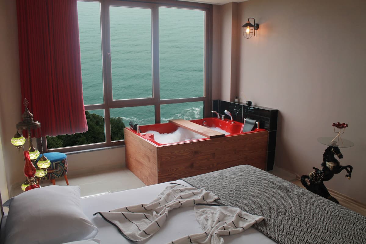 A bedroom with a large window, a wooden bathtub, a bed, and a small table with a decorative horse statue.